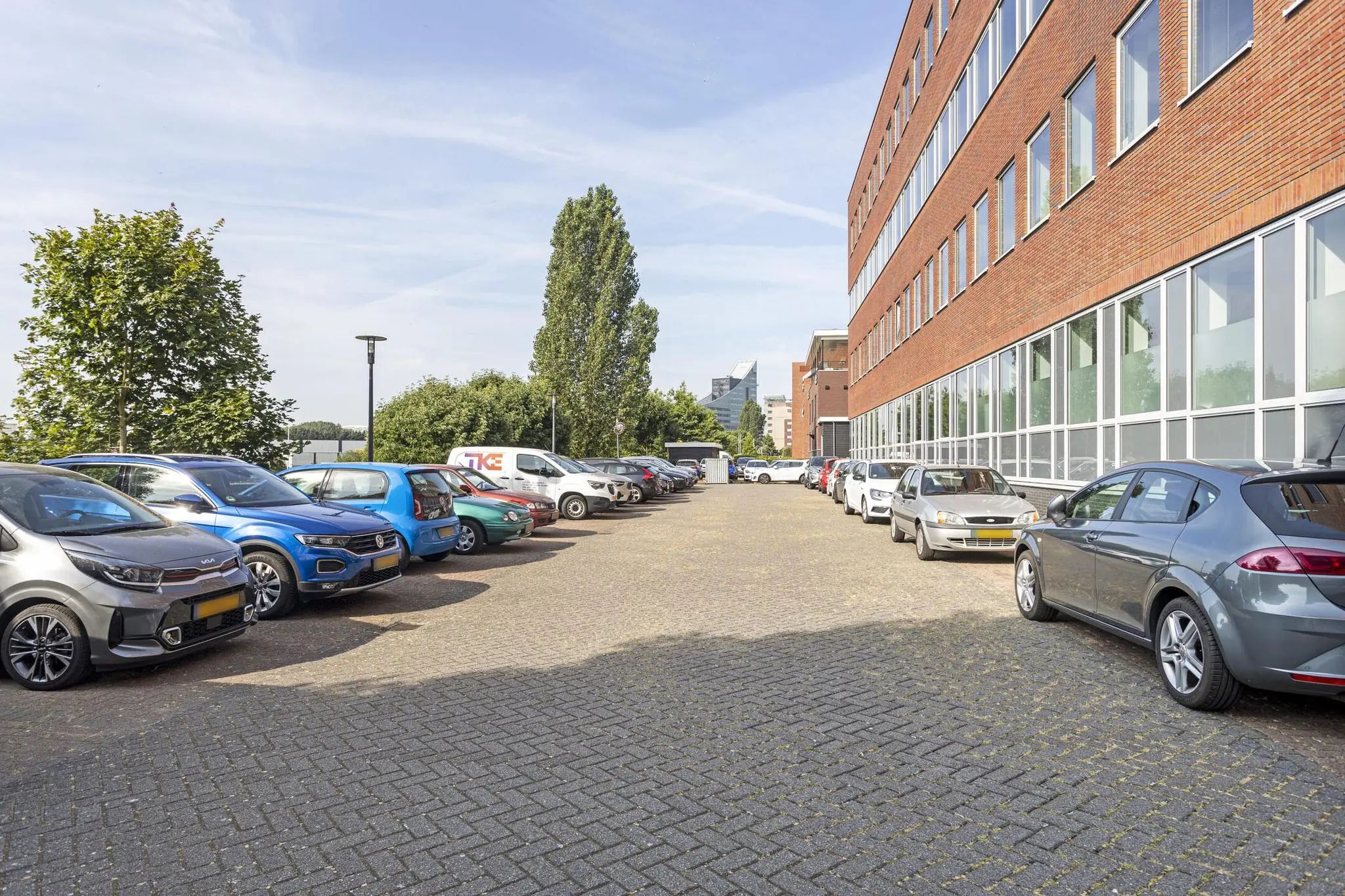 Parkeerterrein met geparkeerde auto's langs een kantoorgebouw aan de Fascinatio Boulevard in een stedelijke omgeving.